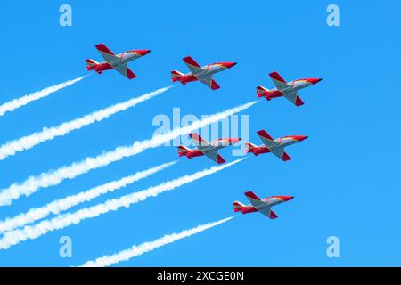 Gijon, Spagna - 24 maggio 2024: Sei caccia a reazione rossi e bianchi volano in formazione, lasciando tracce di fumo contro un cielo azzurro Foto Stock