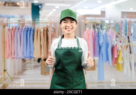 I venditori asiatici indossano grembiule verde e berretto verde sorridenti nel negozio di stoffe Foto Stock