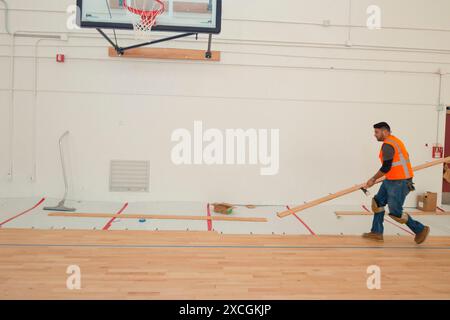 Un lavoratore stabilisce maple pavimenti in legno in un campo di pallacanestro. Foto Stock