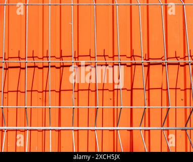 Astratta con schema di una rete metallica sagomata che getta un'ombra su una parete di protezione in metallo verniciata arancione. Sfondo. Foto Stock