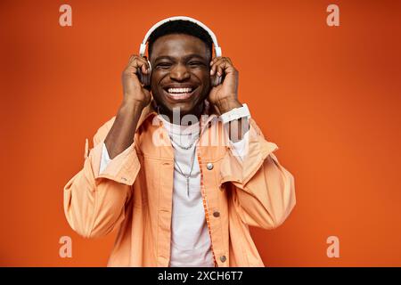 L'elegante uomo nero sorride allegramente indossando le cuffie con un vivace sfondo arancione. Foto Stock