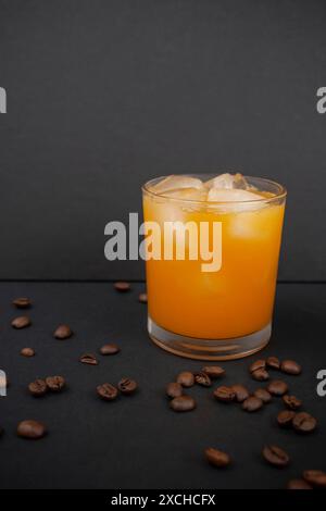 Succo d'arancia con cubetti di ghiaccio in un bicchiere e chicchi di caffè sparsi su sfondo nero Foto Stock