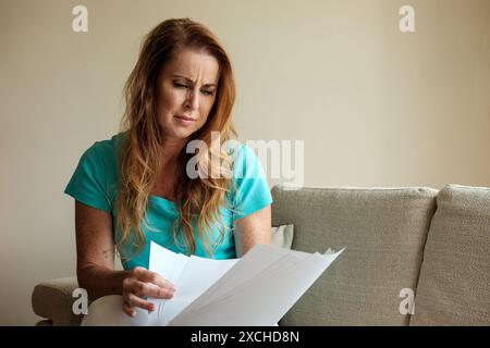 Una donna nei suoi primi anni '40 lotta con un sacco di documenti, preoccupazioni di denaro e lo stress e la preoccupazione dei debiti non pagati. Immagine di crisi del costo della vita Foto Stock