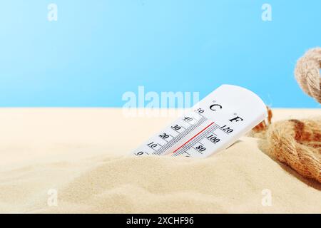 Termometro bianco parzialmente sommerso nella spiaggia di sabbia contro un cielo blu Foto Stock
