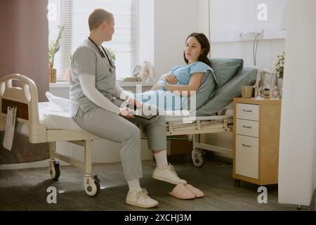 Ostetrico in visita a una giovane donna incinta e avendo una discussione con lei in reparto ospedaliero Foto Stock
