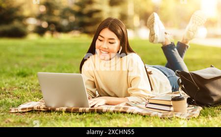 Giovane donna che si rilassa sull'erba con un notebook, che fa i compiti Foto Stock