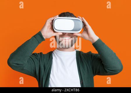 Uomo che indossa Cardigan con le cuffie per realtà virtuale, sfondo arancione Foto Stock