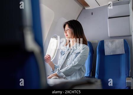Giovane donna turistica che ama viaggiare in aereo, guardare fuori dal finestrino, rilassarsi in un comodo posto a sedere su un aereo moderno Foto Stock