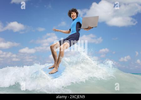 Giovane uomo in muta in sella a una tavola da surf con un computer portatile Foto Stock