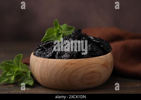 Gustose prugne secche (prugne) e foglie di menta nel recipiente su un tavolo di legno, primo piano Foto Stock