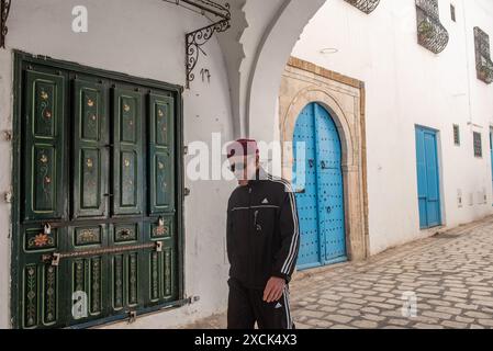 Tunisi, Tunisia 4 maggio 2024 Un tunisino che indossa un cappello rosso chechia nelle bellissime stradine di Tunisi Medina, un quar protetto dal Patrimonio Mondiale dell'Umanità Foto Stock