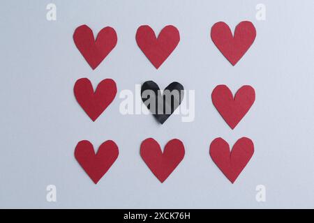 Cuore in carta nera e cuori decorativi rossi su sfondo grigio, piatto. Concetto di problema di relazione Foto Stock