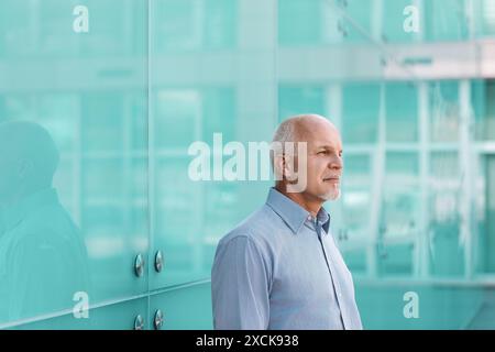 L'uomo d'affari si trova di fronte a un moderno edificio di uffici, profondamente preoccupato del potenziale impatto della tecnologia sulla società Foto Stock