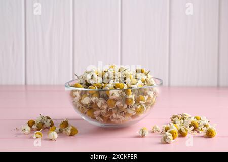 Fiori di camomilla in una ciotola di vetro su un tavolo di legno rosa Foto Stock