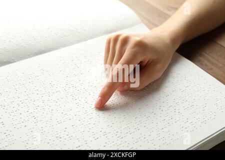 Donna cieca che legge un libro scritto in Braille a un tavolo di legno, primo piano Foto Stock