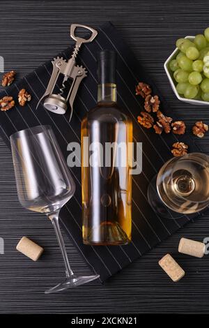 Cavatappi, bottiglia di vino, bicchieri, sugheri, noci e uva sul tavolo nero, vista dall'alto Foto Stock
