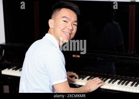 Un adolescente asiatico sta suonando felicemente un pianoforte a casa, guardando indietro la macchina fotografica con un sorriso sul suo volto Foto Stock