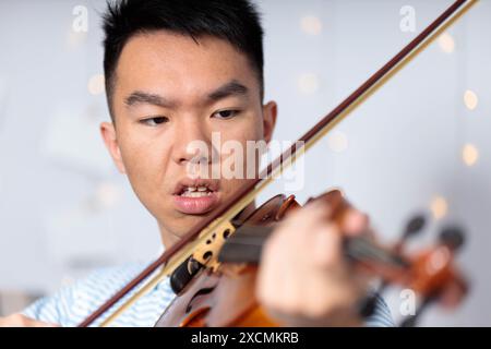 Primo piano di un giovane adolescente asiatico che suona il violino, il suo volto pieno di concentrazione e concentrazione mentre si pratica Foto Stock