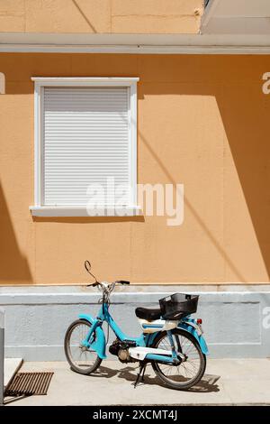 Ciclomotore blu vintage parcheggiato da una parete gialla brillante Foto Stock