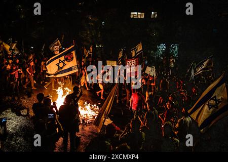 Gerusalemme, Israele. 17 giugno 2024. I manifestanti tengono cartelli e le bandiere israeliane accanto a un falò durante una dimostrazione. I manifestanti anti anti-governativi israeliani si sono radunati a Gerusalemme, alcuni si sono scontrati con la polizia vicino alla casa del primo ministro Benjamin Netanyahu chiedendo nuove elezioni e un accordo con Hamas. Credito: SOPA Images Limited/Alamy Live News Foto Stock