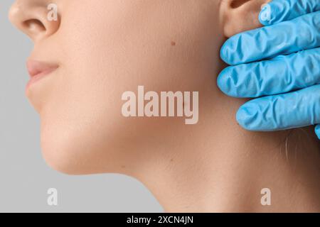 Dermatologo che esamina le talpe sul viso della donna su sfondo grigio, primo piano Foto Stock