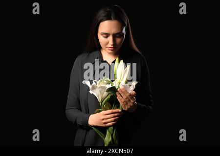Giovane donna con bouquet funebre di fiori di giglio su sfondo nero Foto Stock