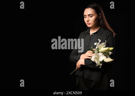 Giovane donna con bouquet funebre di fiori di giglio su sfondo nero Foto Stock