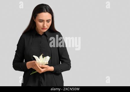 Giovane donna con fiori di giglio funebre su sfondo bianco Foto Stock