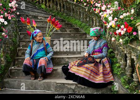 Donna Hmong di fiori seduta sulle scale del Palazzo dei Re Hmong (Vau Meo) a Bac ha, provincia di Lao Cai, Vietnam Foto Stock