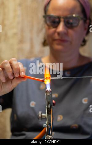 Artigiana che crea un gioiello di vetro nella sua bottega Foto Stock