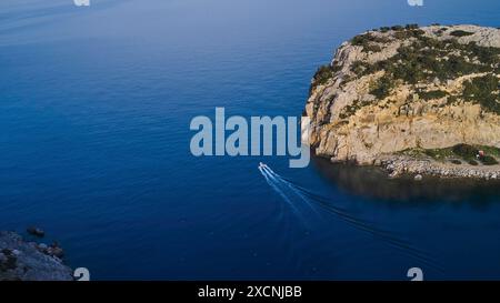 Colpo di droni, piccola barca che naviga attraverso le acque cristalline lungo una ripida scogliera, Anthony Quinn Bay, Vagies Bay, Rodi, Dodecaneso, isole greche Foto Stock