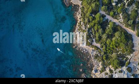 Colpo di droni, acque cristalline lungo una costa con vegetazione fitta, una piccola barca, Anthony Quinn Bay, Vagies Bay, Rodi, Dodecaneso, Isole greche Foto Stock