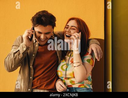 Due amici gioiosi che si divertono a parlare al telefono, condividendo le risate fuori in una giornata di sole. Foto Stock