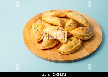 Torte di samsa appena sfornate con carne cosparsa di semi di papavero su un piatto di legno, cucina dell'asia centrale Foto Stock