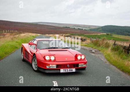 Una Ferrari Testarossa degli anni '80 con i suoi fari pop-up in piedi su una strada di campagna nello Yorkshire Peak District con le brughiere alle spalle Foto Stock