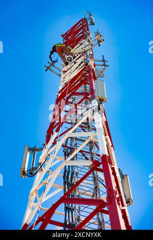 operaio tecnico su un'antenna cellulare a torre, sfondo cielo chiaro Foto Stock