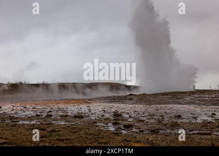 Geyser Strokkur in eruzione, geyser tipo fontana nell'area geotermica in Islanda, persone che guardano sullo sfondo. Foto Stock