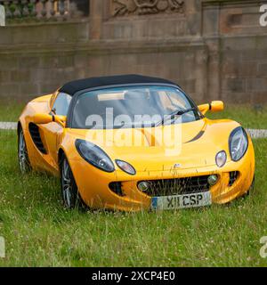 Yellow Lotus Elise S2 parcheggiata su erba con un muro di pietra dietro Foto Stock