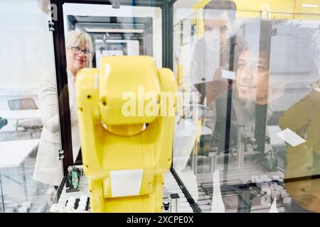 Gli ingegneri esaminano da vicino le funzionalità di un braccio robotico giallo durante una sessione di formazione pratica in un ambiente industriale. Foto Stock