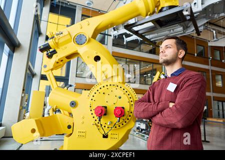 Ingegnere professionista che supervisiona un robot industriale avanzato con braccio di presa meccanico in un ambiente di produzione high-tech Foto Stock