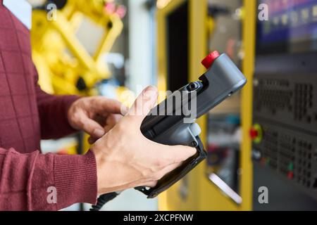 Primo piano di un tecnico che utilizza un pannello di controllo per programmare un braccio robotizzato. Ideale per illustrare robotica, automazione industriale e tecnologia di produzione Foto Stock