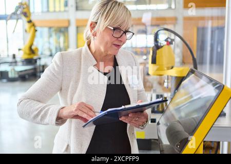 Ingegnere donna che progetta un robot industriale con braccio di presa in un ambiente di fabbrica moderno, incentrato sull'automazione e sullo sviluppo robotico. Foto Stock