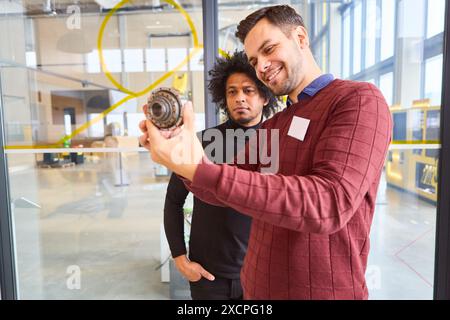 Due ingegneri che esaminano e discutono di un componente robotico in un laboratorio moderno, evidenziando l'automazione industriale e lo sviluppo della tecnologia robotica Foto Stock