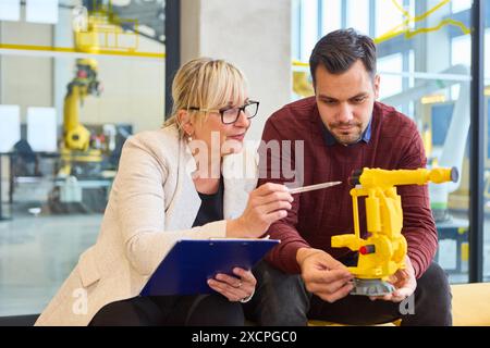 Due ingegneri che collaborano alla progettazione e alla funzionalità di un braccio robotizzato in un laboratorio industriale, focalizzati sulla produzione e l'automazione Foto Stock