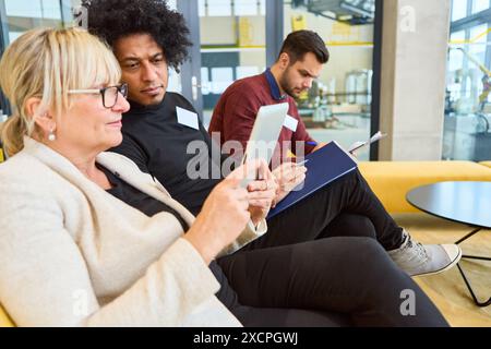 Diversi gruppi di professionisti che collaborano a un progetto utilizzando un tablet e documenti in un ambiente di ufficio moderno. Foto Stock