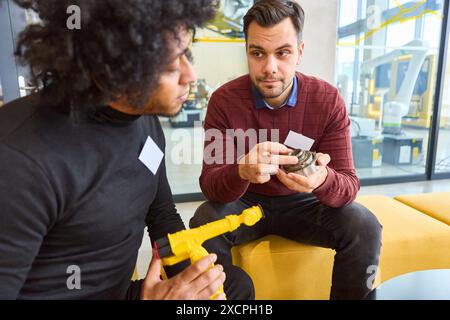 Due ingegneri esaminano e discutono parti di un braccio robotico in un ambiente industriale avanzato, concentrandosi sulla tecnologia e l'innovazione. Foto Stock