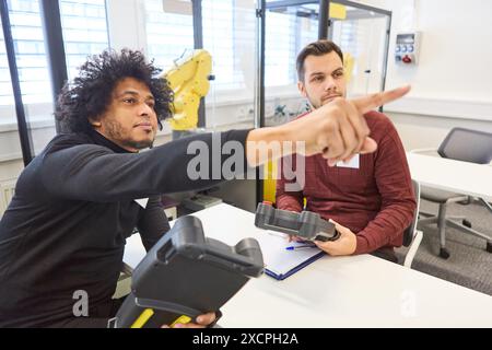 Due ingegneri che collaborano alla formazione sulla robotica, lavorando con i controller del braccio di presa in un ambiente industriale. Si concentrano sulla programmazione A. Foto Stock