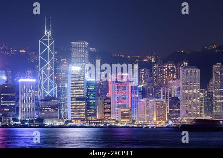 Fantastica vista notturna dello skyline dell'Isola di Hong Kong dal lato di Kowloon. Grattacieli in centro. Luci colorate della città riflesse nell'acqua del porto Victoria. Foto Stock