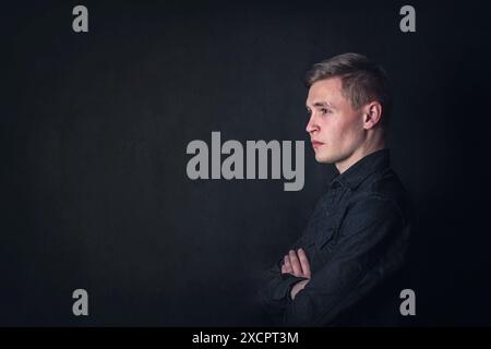 Ritratto con vista laterale di un giovane contemplativo serio, con un aspetto penoso su uno sfondo scuro della parete. Lo studente maschile riflette come le domande Foto Stock