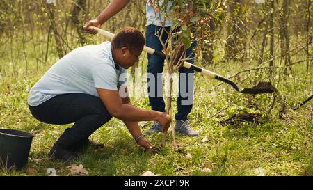 Attivisti afroamericani piantano alberi per la conservazione della natura, contribuendo alla sostenibilità e alla conservazione dell'ecosistema. Team di volontari che si uniscono per la cura dell'ambiente, semi di piante. Telecamera A.. Foto Stock